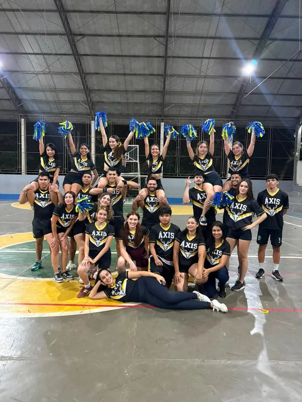 A equipe de uniforme com pompons levantados, numa quadra